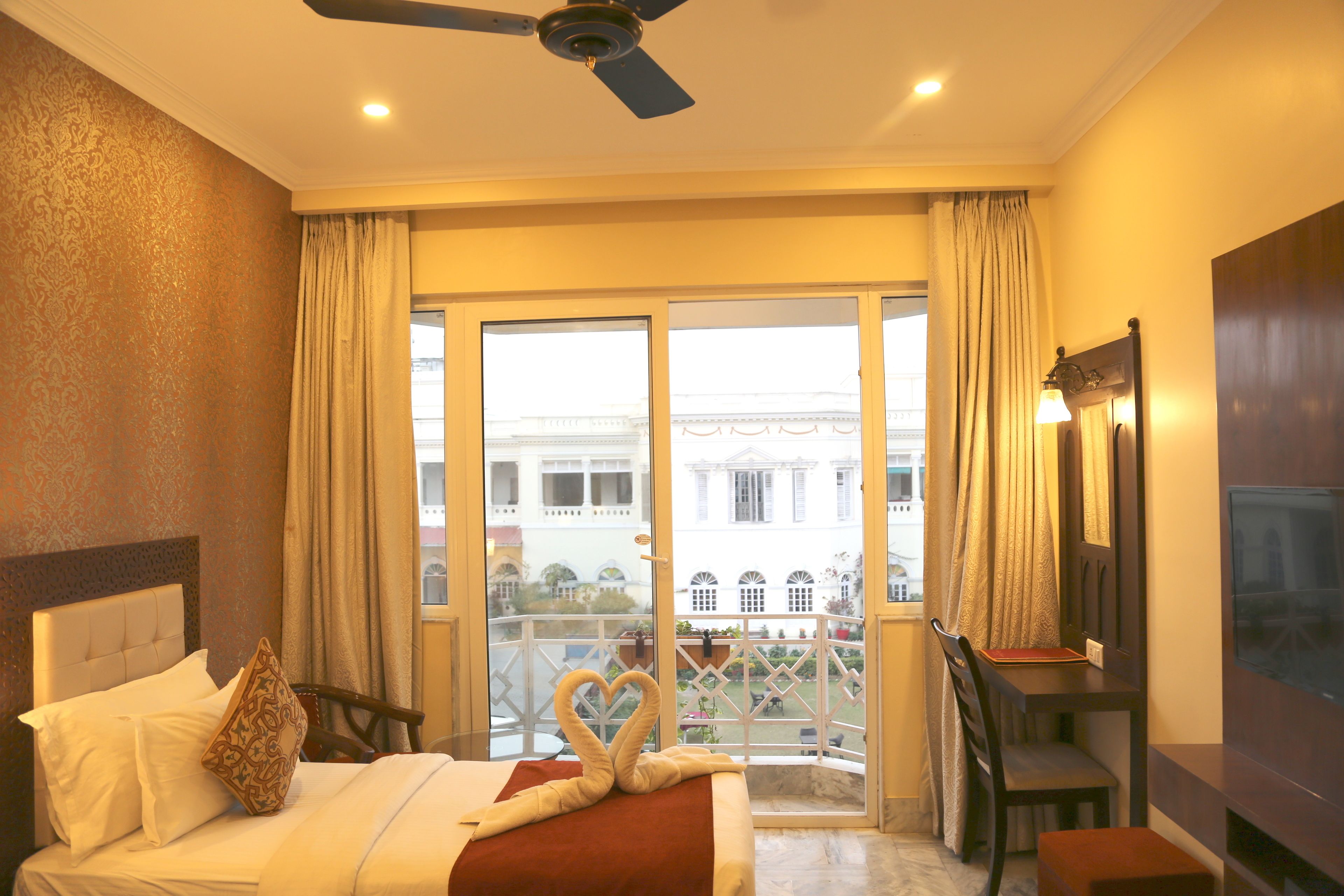 Camera d'albergo con un letto, una scrivania, una sedia, una TV e un balcone con vista sugli edifici.