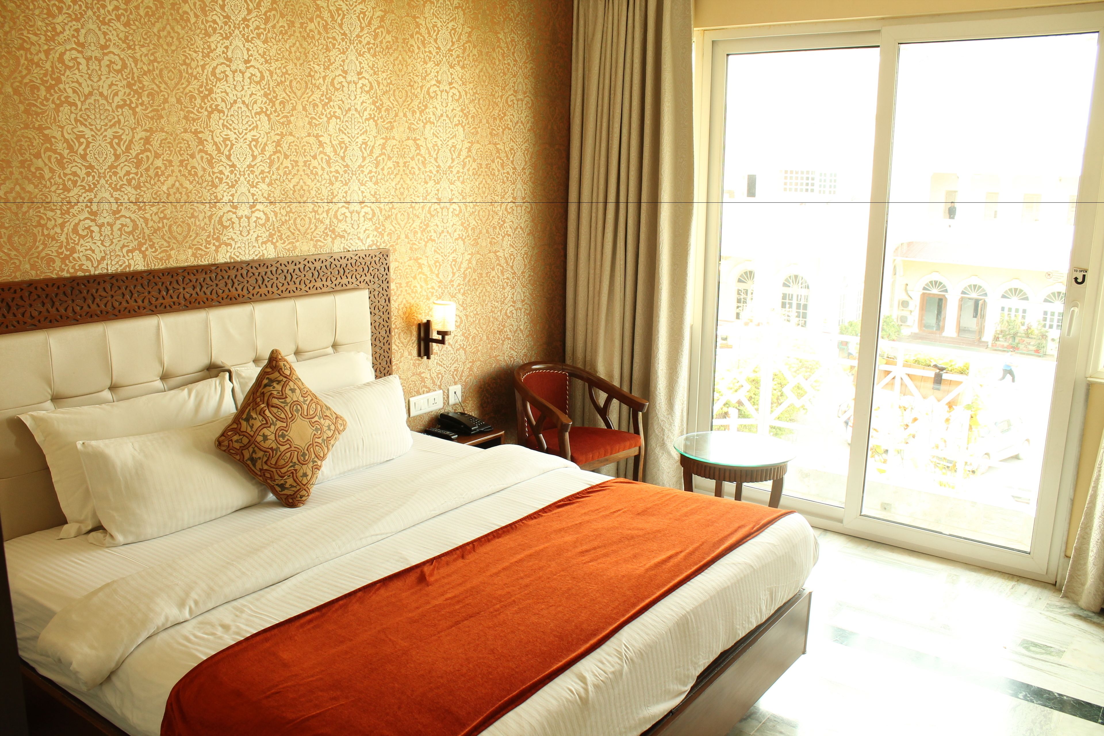 Quarto de hotel com uma cama grande, uma mesa pequena, uma cadeira e vista para o exterior.
