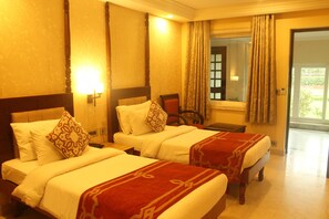 A hotel room with two beds, a nightstand, a chair, and a window with curtains. - Hotel Surya (Varanasi)