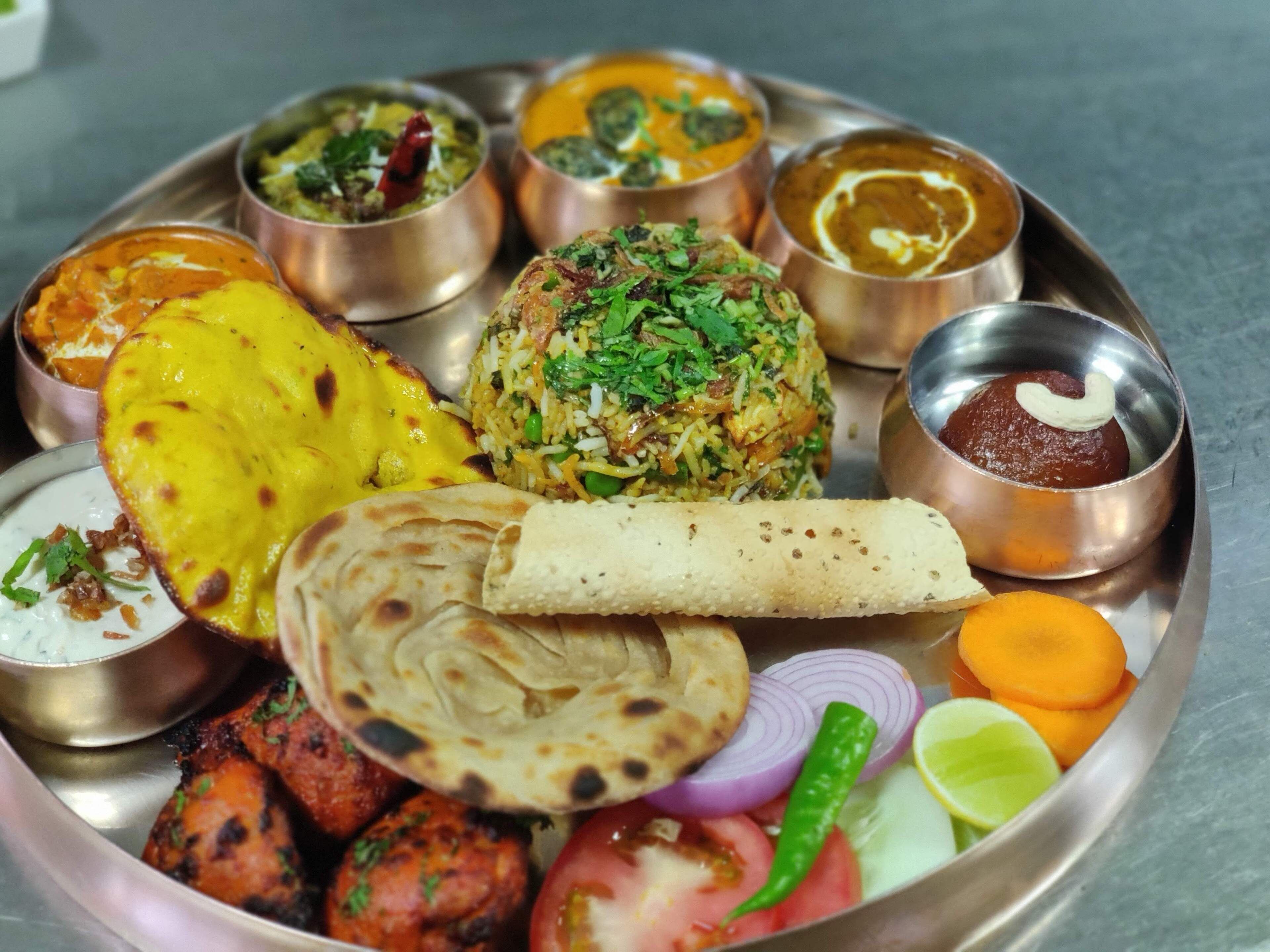 Un repas traditionnel indien composé de différents plats, notamment du poulet tandoori, du pain naan et une variété de plats en sauce et de plats à base de riz.