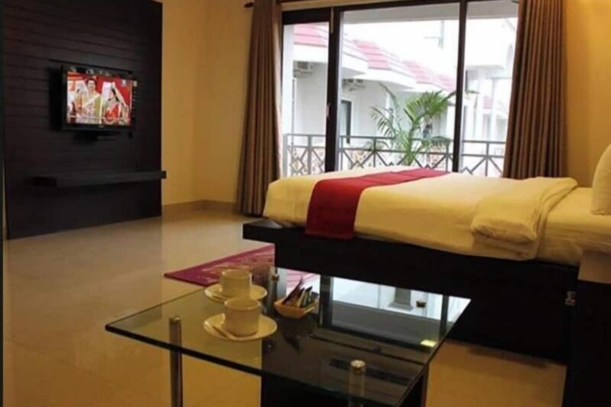 A hotel room with a bed, a television, a glass coffee table, and a view of the outside.