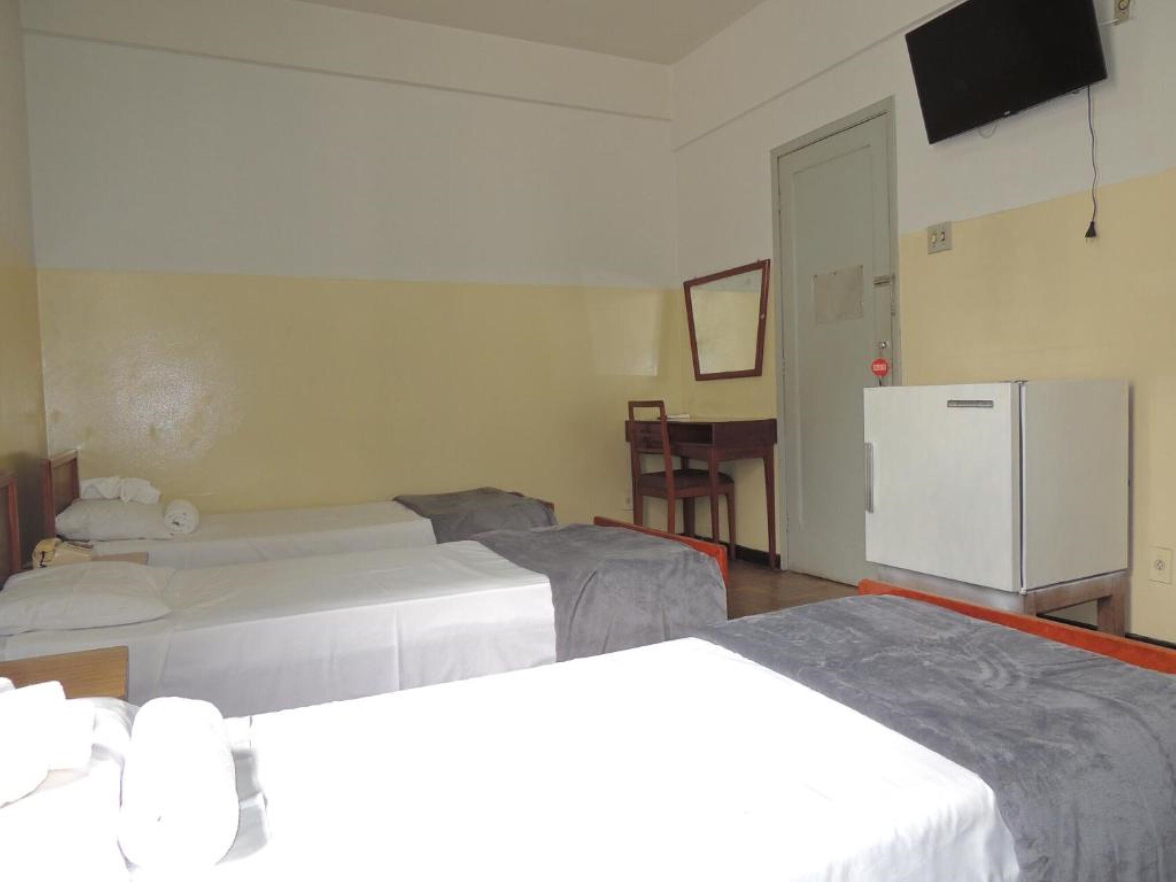 Hotellihuone, jossa on kaksi sänkyä, työpöytä, tuoli, televisio ja jääkaappi.