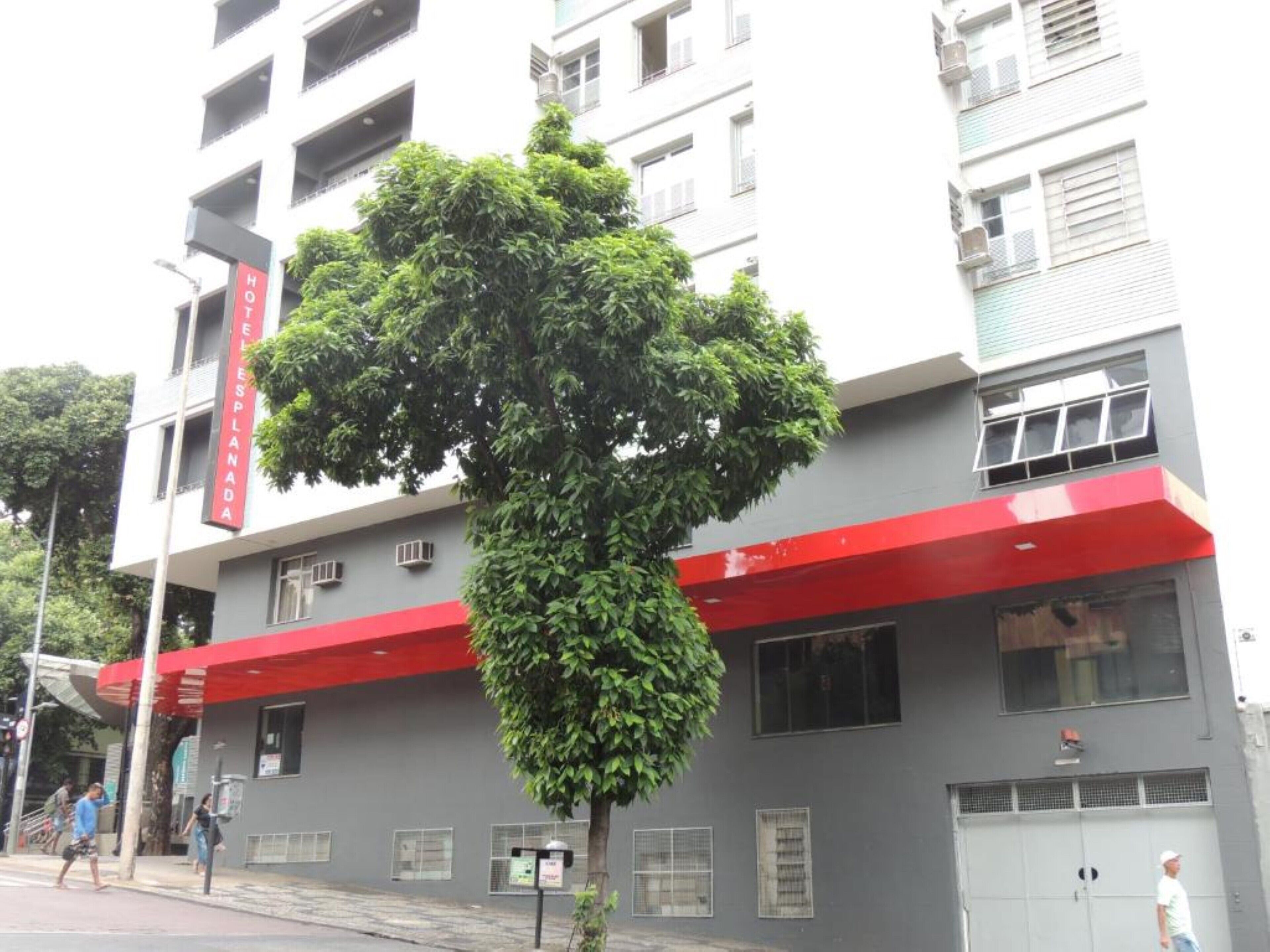 A hotel with a red awning and a tree in front.