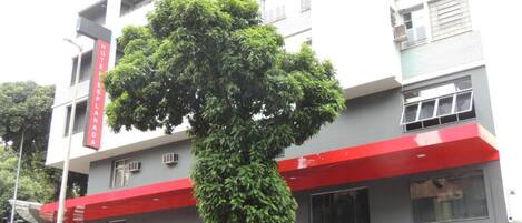 A hotel with a red awning and a tree in front.
