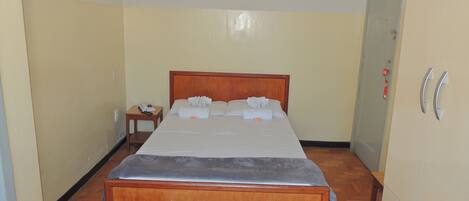 Quarto de hotel com cama de madeira, mesa de cabeceira com telefone e guarda-roupa com espelho.