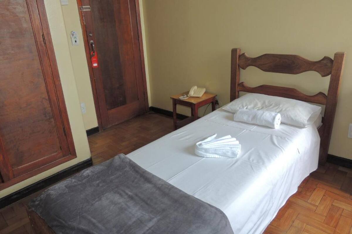 Habitación de hotel con cama de madera, mesita de noche con teléfono y puerta con detector de incendios.