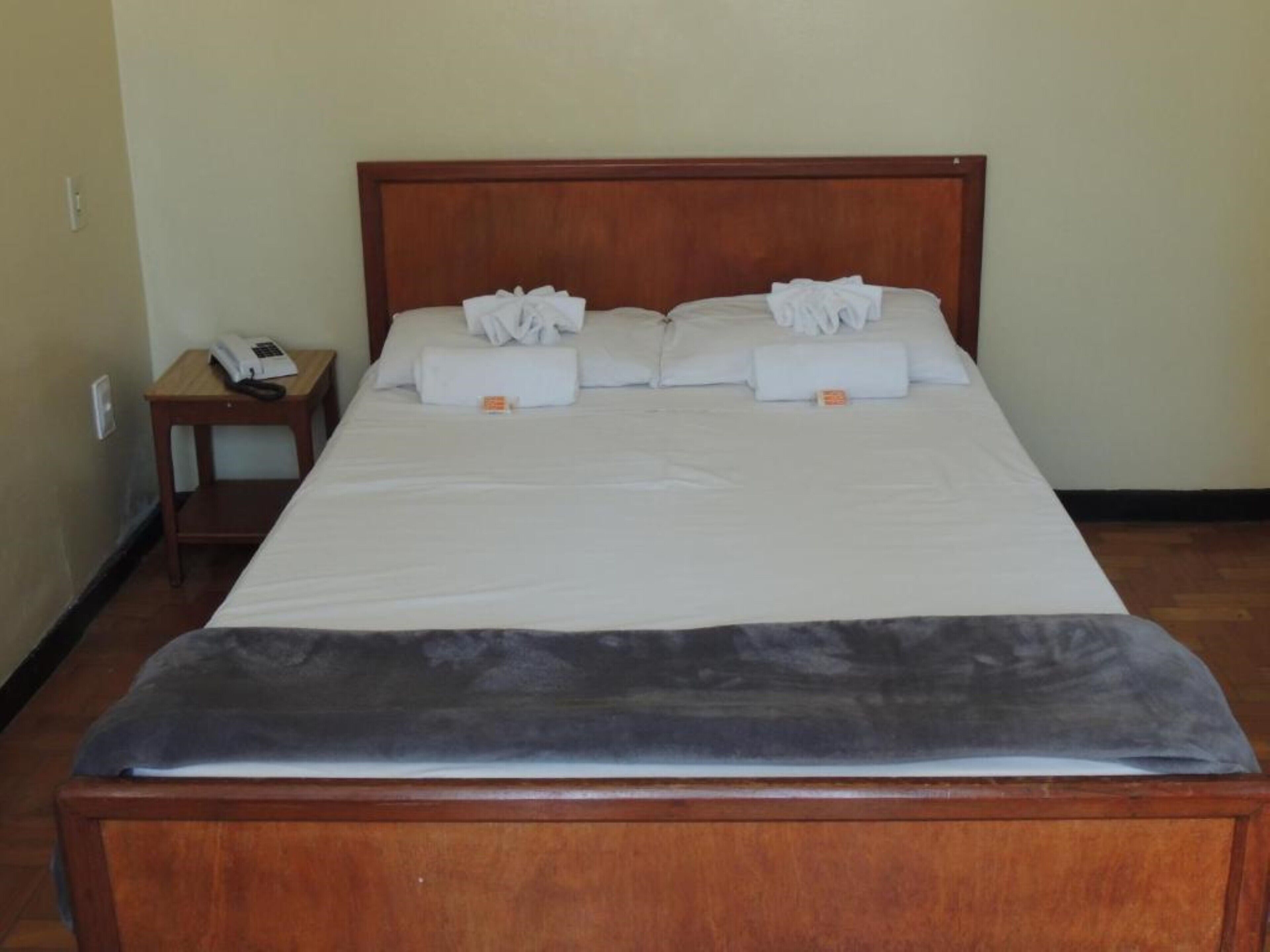 A neatly made bed with white linens and towels, a wooden headboard, and a small bedside table with a telephone.