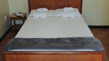 Cama bem arrumada com lençóis e toalhas brancos, cabeceira de madeira e uma pequena mesa de cabeceira com telefone.