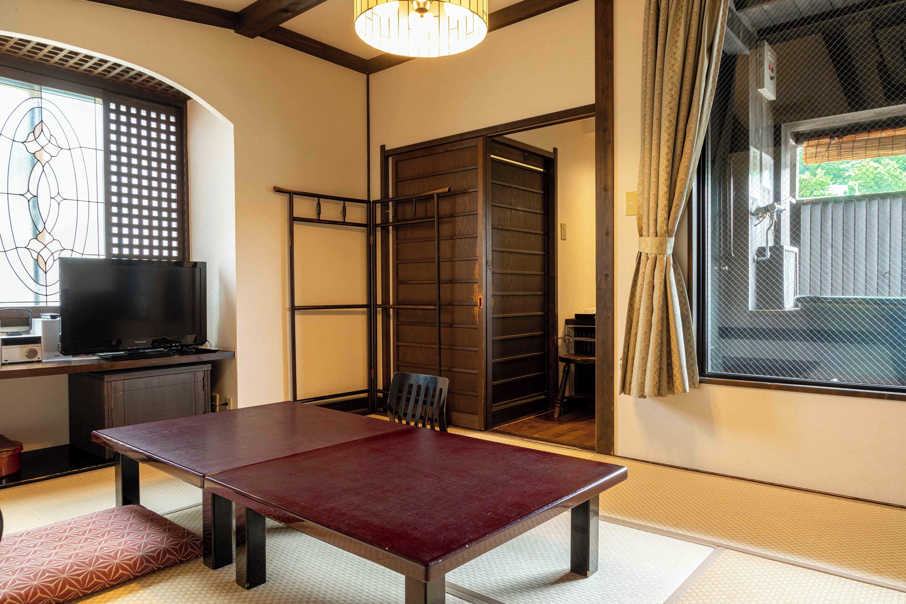 Una habitación japonesa tradicional con suelo de tatami, una mesa baja, un televisor y una puerta corredera que da a un espacio exterior.