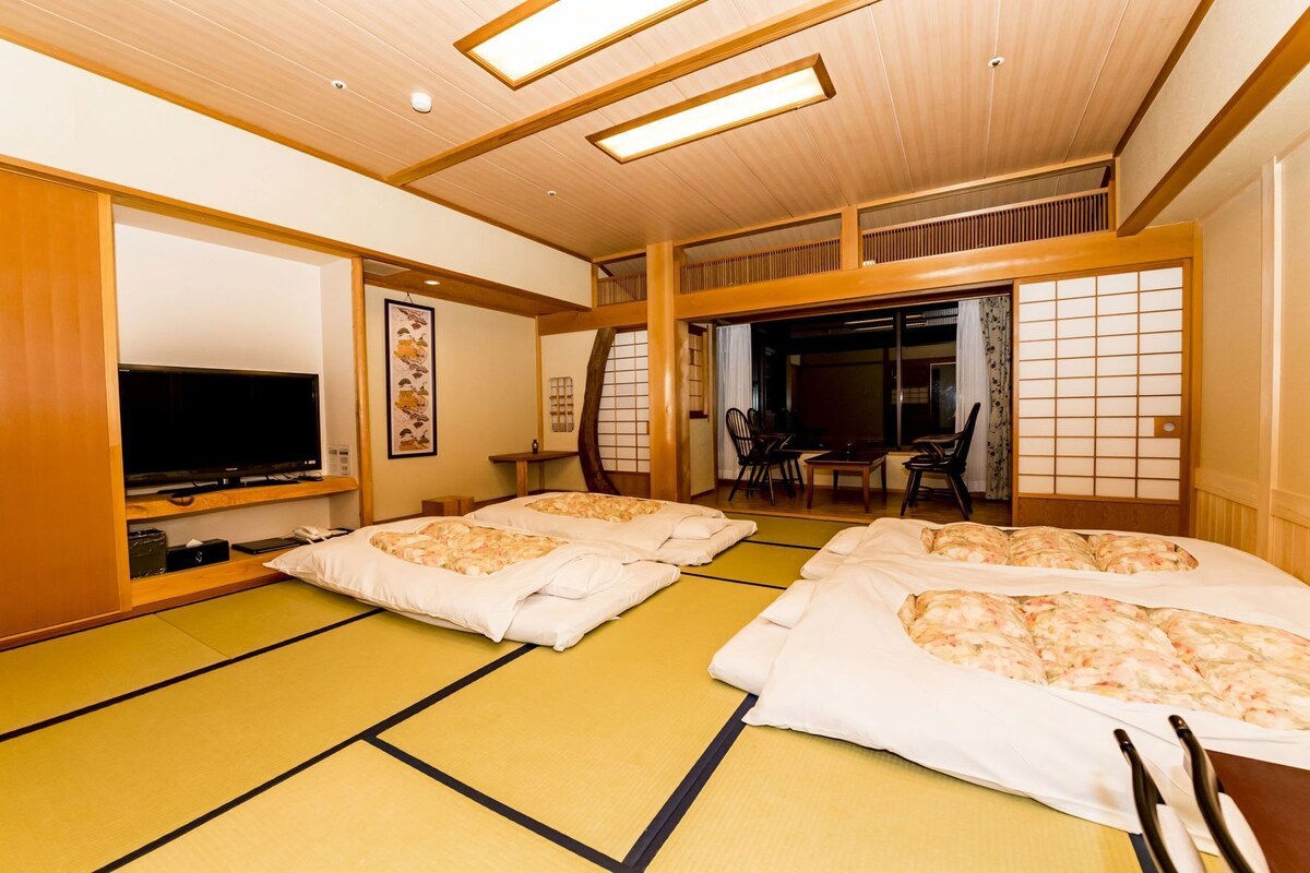 A traditional Japanese room with tatami flooring, a television, and a dining area with sliding doors.