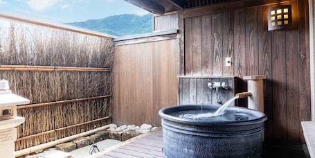 A wooden spa area with a large stone hot tub, bamboo wall, and a view of mountains.. Sasara Gero Hot Springs