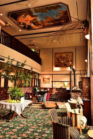 A spacious lobby with a high ceiling, a large painting, and a seating area with multiple chairs and tables.