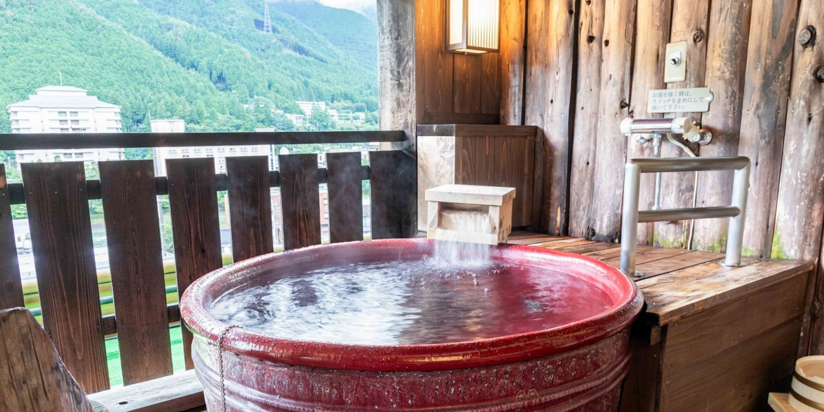 A hot spring bath area with a wooden deck and a view of a mountainous landscape.