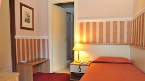 A hotel room with a single bed, a bedside table with a lamp, a telephone, and a small desk with a chair. - Catania Centro Rooms (Catania)