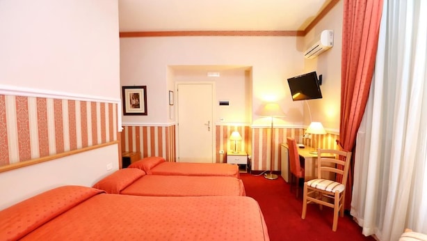 A hotel room with three beds, a desk, a chair, a TV, and a window with curtains. - Catania Centro Rooms (Catania)