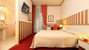 A hotel room with a bed, a bedside table with a lamp, a telephone, a red carpet, a bathroom with a sink and mirror, and a TV mounted on the wall. - Catania Centro Rooms (Catania)