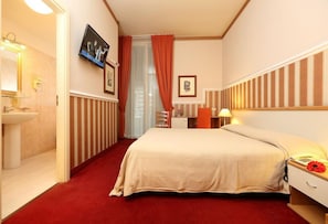A hotel room with a bed, a bedside table with a lamp, a telephone, a red carpet, a bathroom with a sink and mirror, and a TV mounted on the wall. - Catania Centro Rooms (Catania)