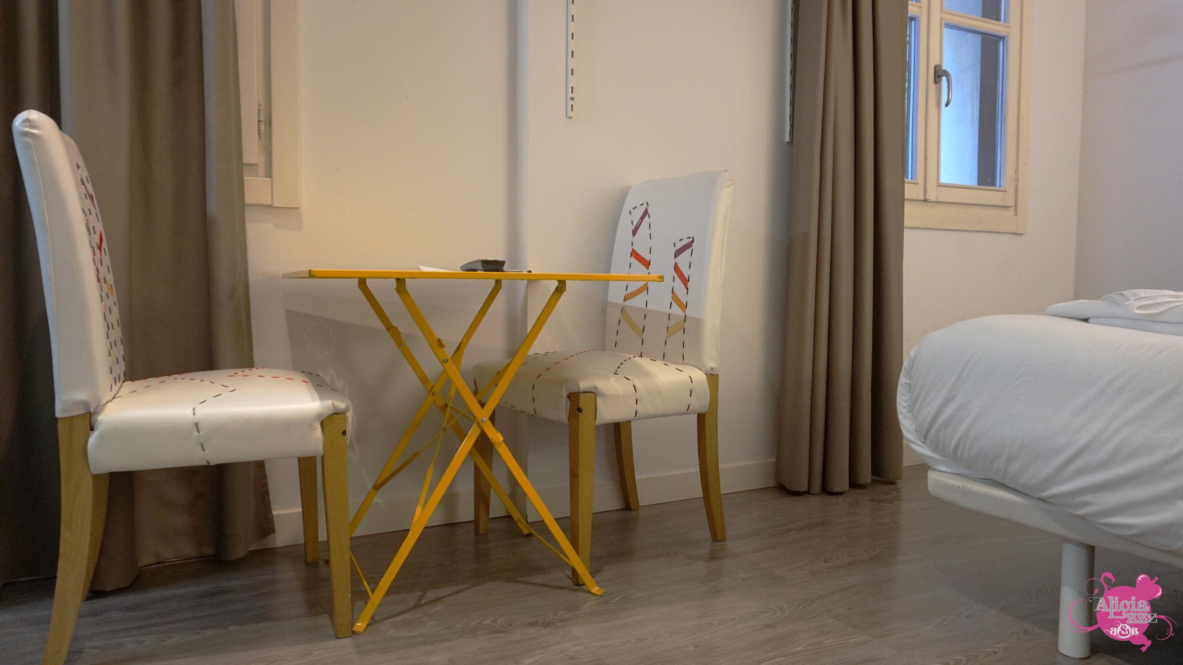 A room with a bed, two chairs, a small table, and a window with curtains.