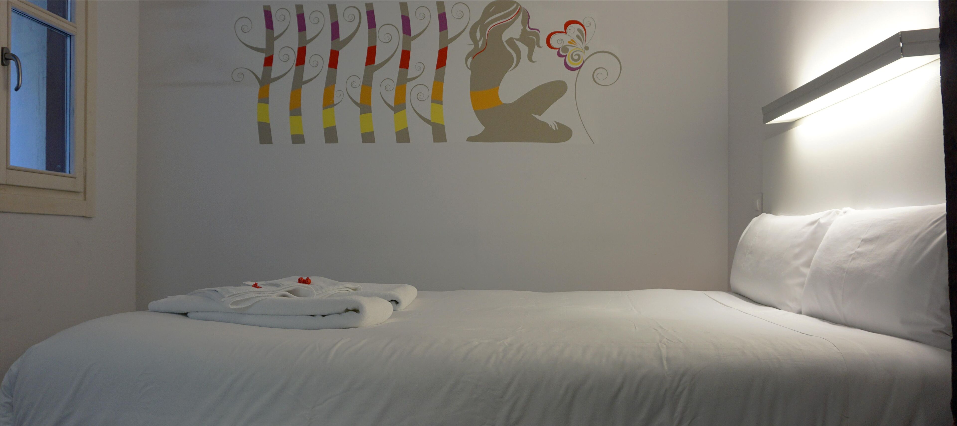 Een slaapkamer met een bed, wanddecoratie van bomen en een figuur, en een raam met uitzicht.