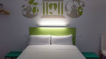 Een opgemaakt bed met witte lakens, een groen hoofdeinde en een nachtkastje met een groen oppervlak.