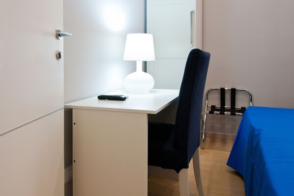 Una habitación de hotel con escritorio, silla, lámpara y una mesa con mantel azul.