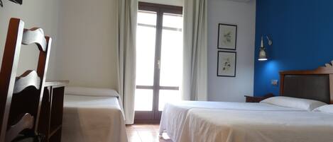 Habitación de hotel con dos camas, una silla de madera, un escritorio, una lámpara y una ventana con cortinas.