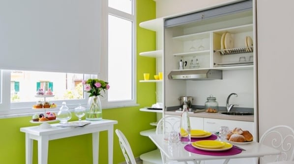 A bright kitchen with white cabinetry, a dining table with yellow plates, and a window with a view of greenery.