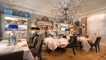 A dining area with tables set for four, elegant chandeliers, and a brick wall.