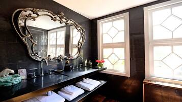 A bathroom with a large ornate mirror, a black countertop, a sink, and a window with a geometric pattern.