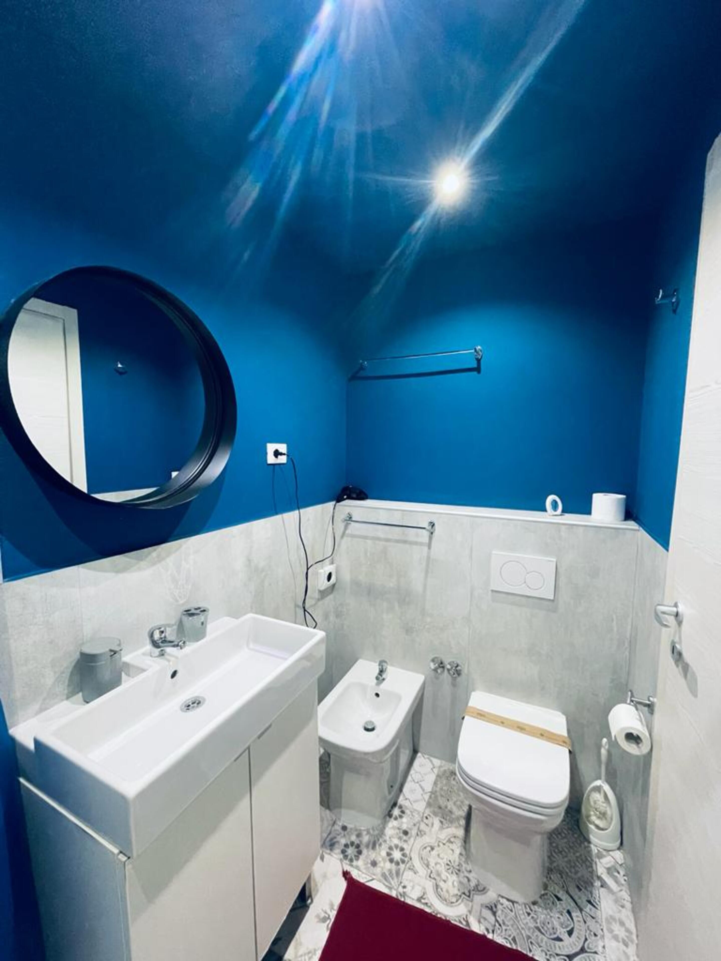 Un bagno con un lavandino bianco, un piccolo WC e un bidet. C'è uno specchio a parete e un portascopino sopra il water.