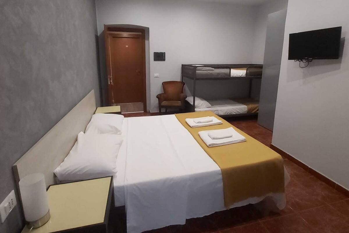 Una habitación de hotel con cama, una silla, televisor y puerta.