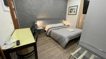 A compact bedroom with a bed, bedside table, and a small desk with a chair.