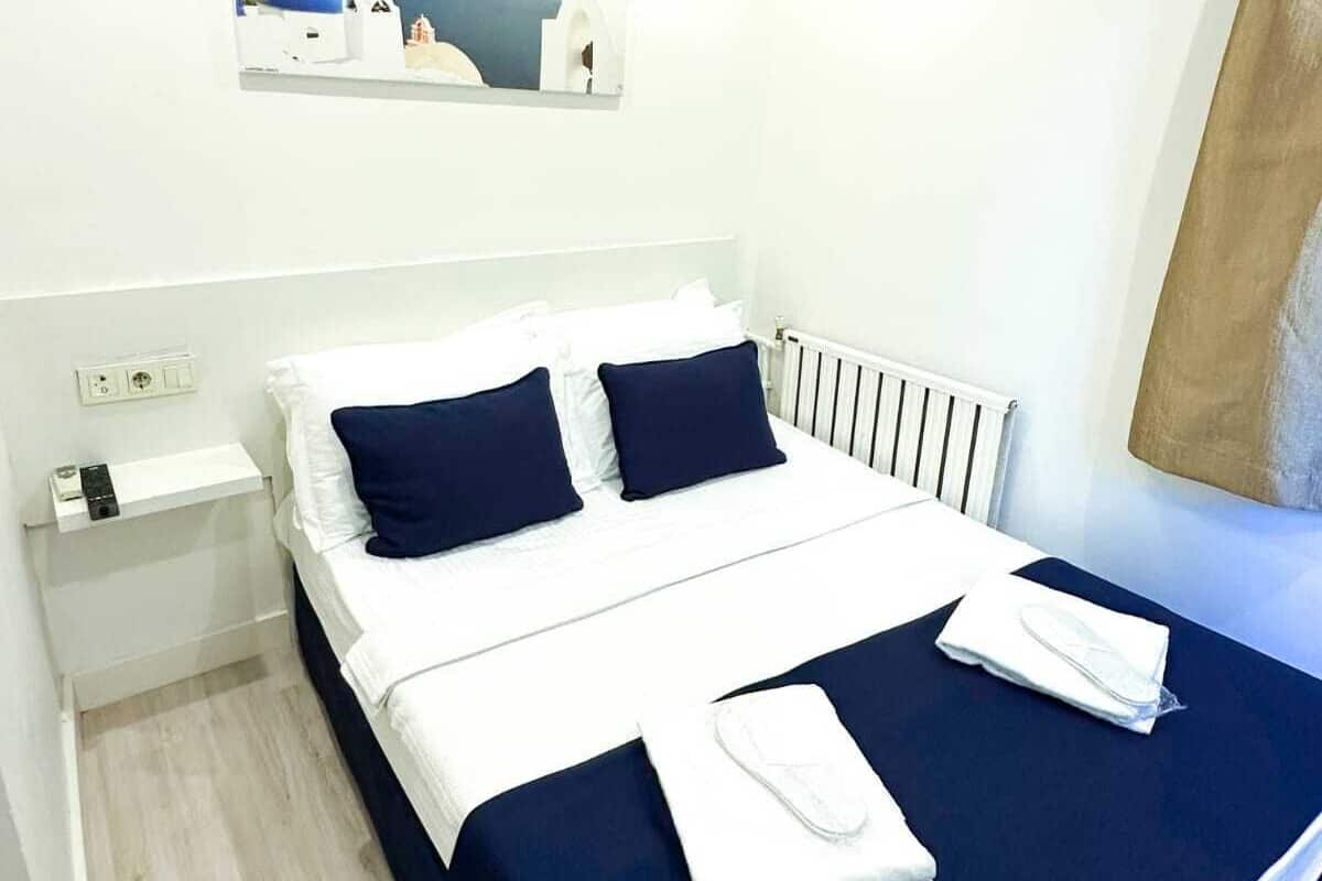 Ein modernes Hotelzimmer mit einem großen Bett, weißen Wänden, einem Gemälde einer Küstenlandschaft und einem Fenster mit Blick.