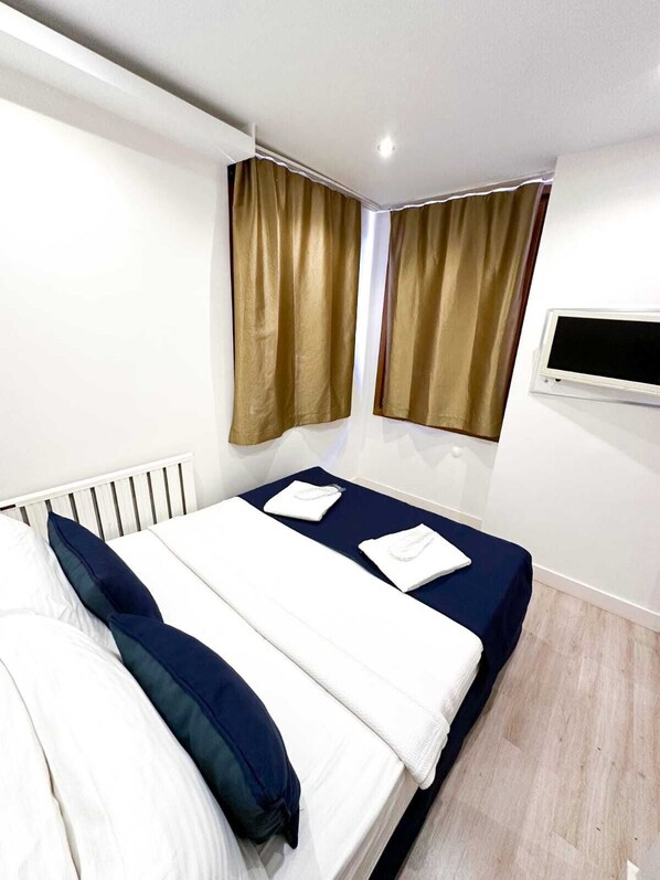 A hotel room with a bed, two windows with curtains, a TV mounted on the wall, and a white radiator. - Büyükada Comfort Hotel (Adalar)