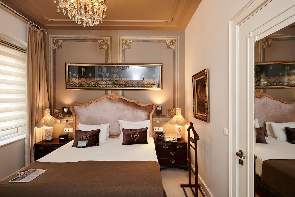 A well-appointed hotel room with a large bed, two bedside tables, a nightstand, a chandelier, and a large mirror.
