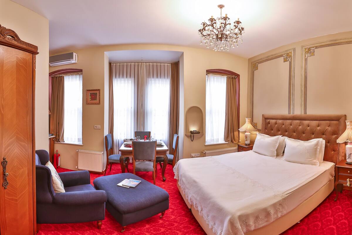 A hotel room with a large bed, a dining table, and a chandelier.
