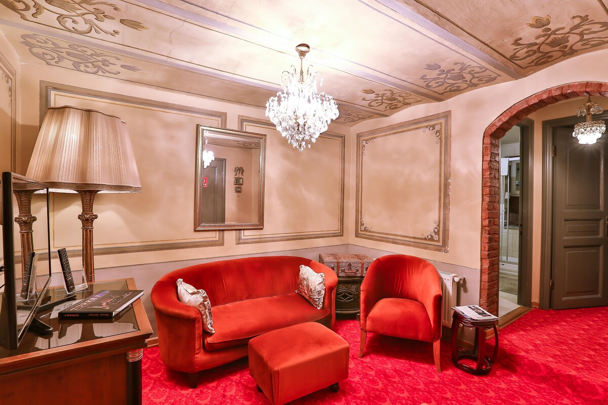 A room with a red sofa, a small table, a lamp, and a chandelier.