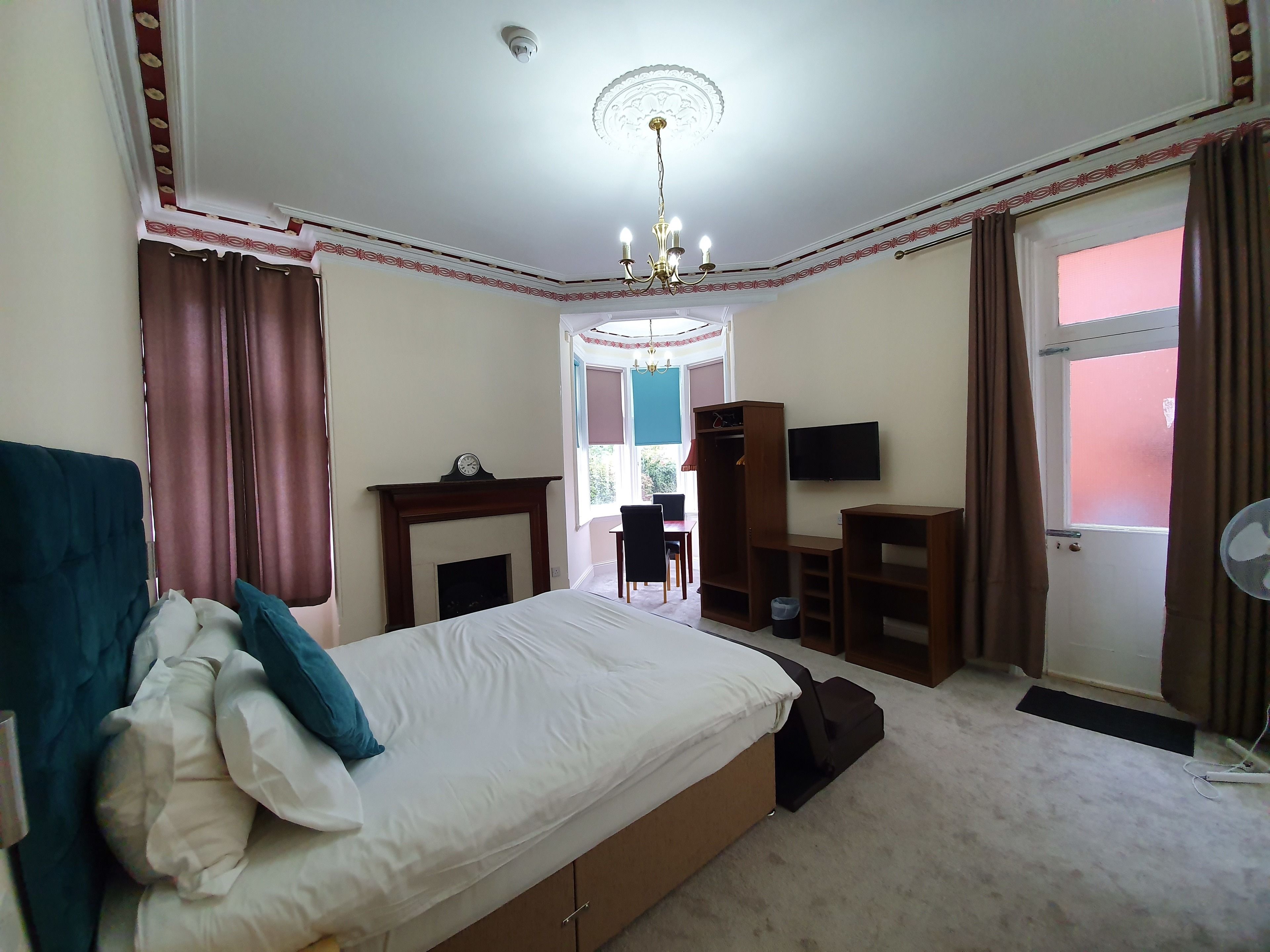 A bedroom with a bed, a wardrobe, a desk, a chair, a television, and a window with curtains.