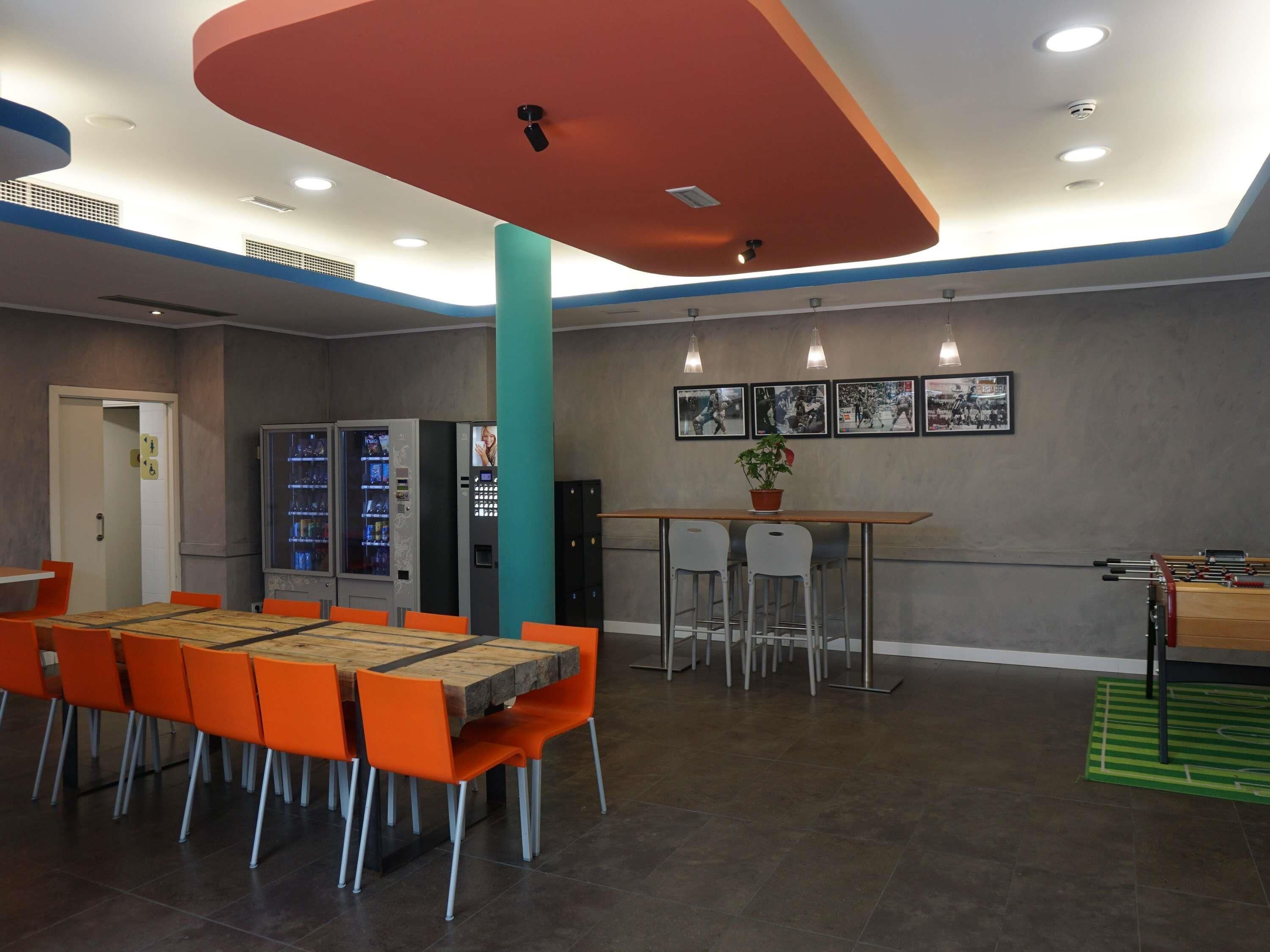 Een eetgedeelte met een houten tafel, oranje stoelen, automaten en een tafelvoetbaltafel.