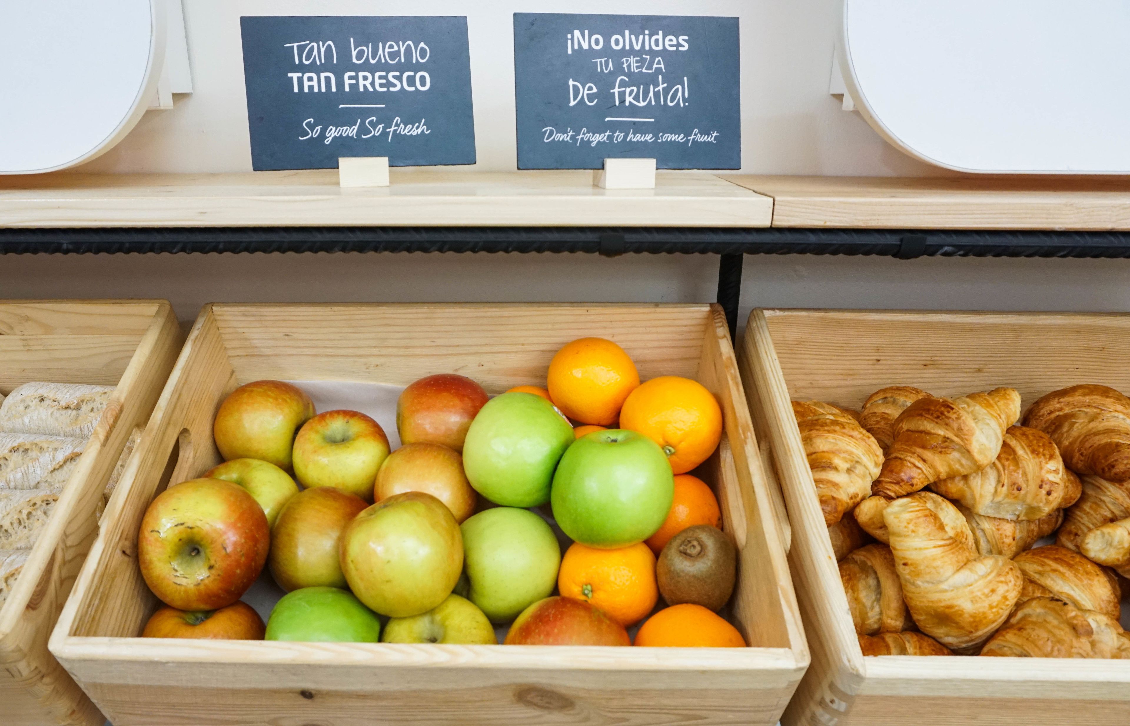 A display of fresh fruits and pastries in wooden crates with signs in Spanish.