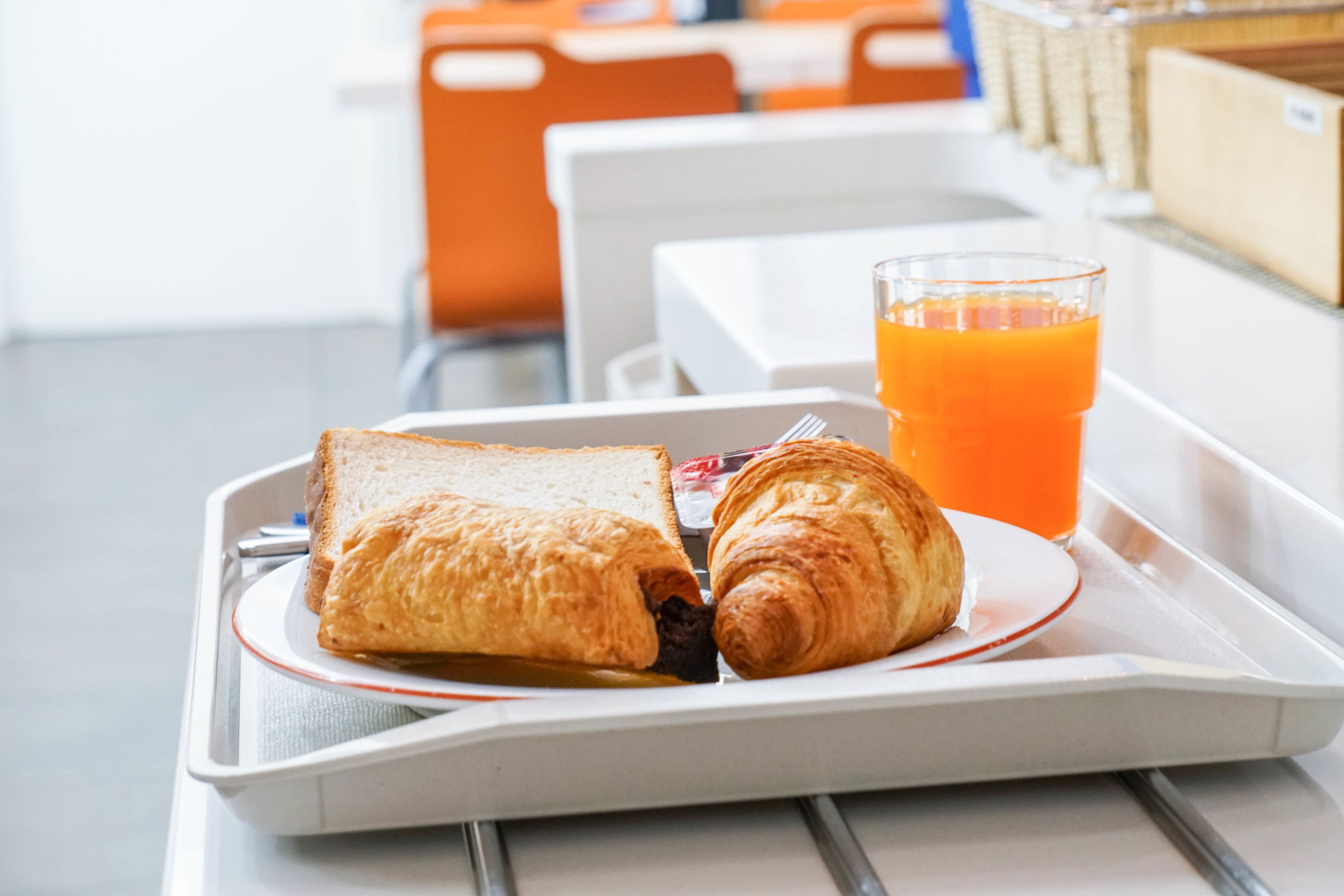 A tray with a croissant and a sandwich, and a glass of orange juice.