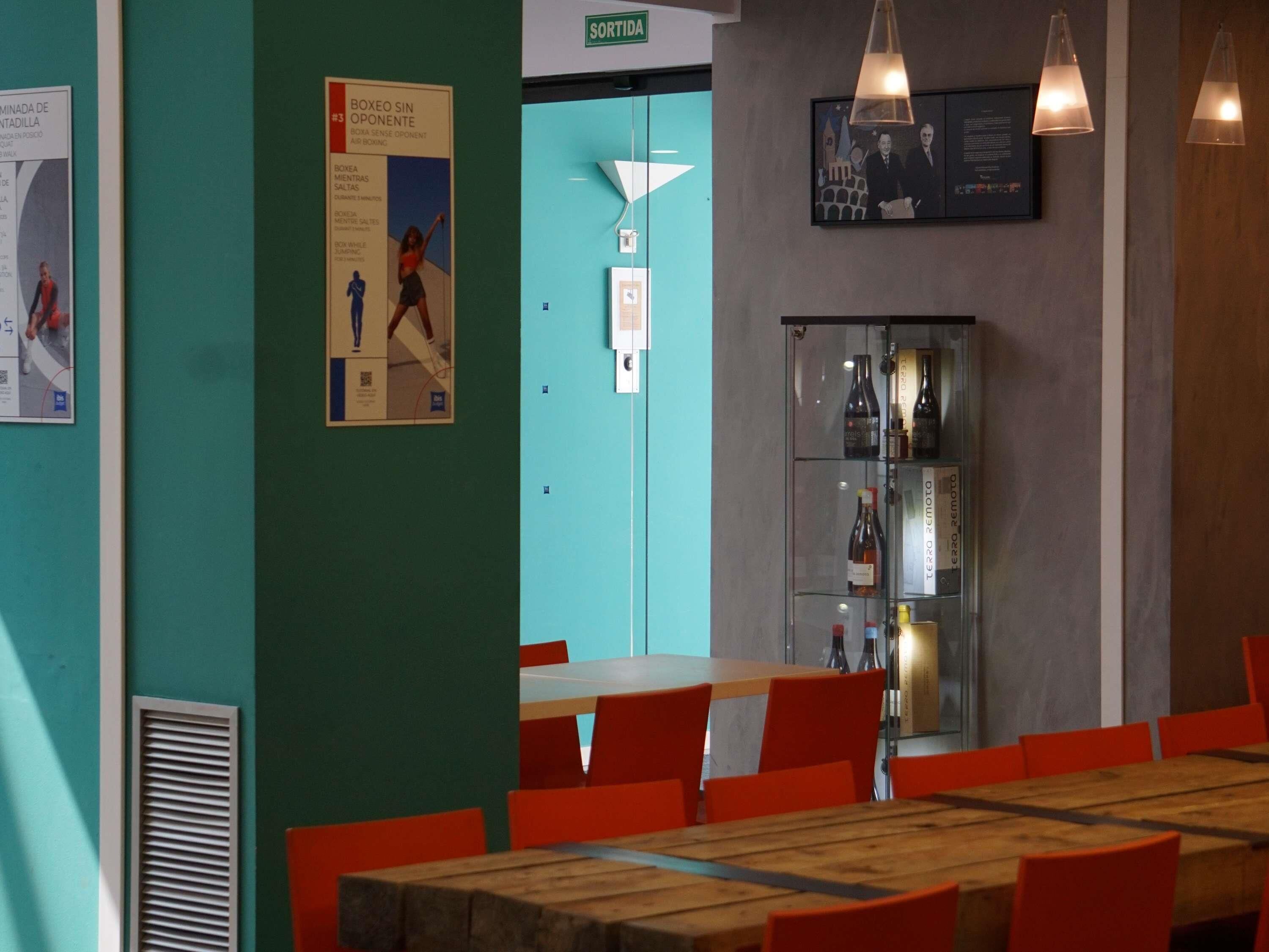 A conference room with a wooden table and orange chairs, a glass cabinet with bottles, and a door labeled 'SORTIDA'.
