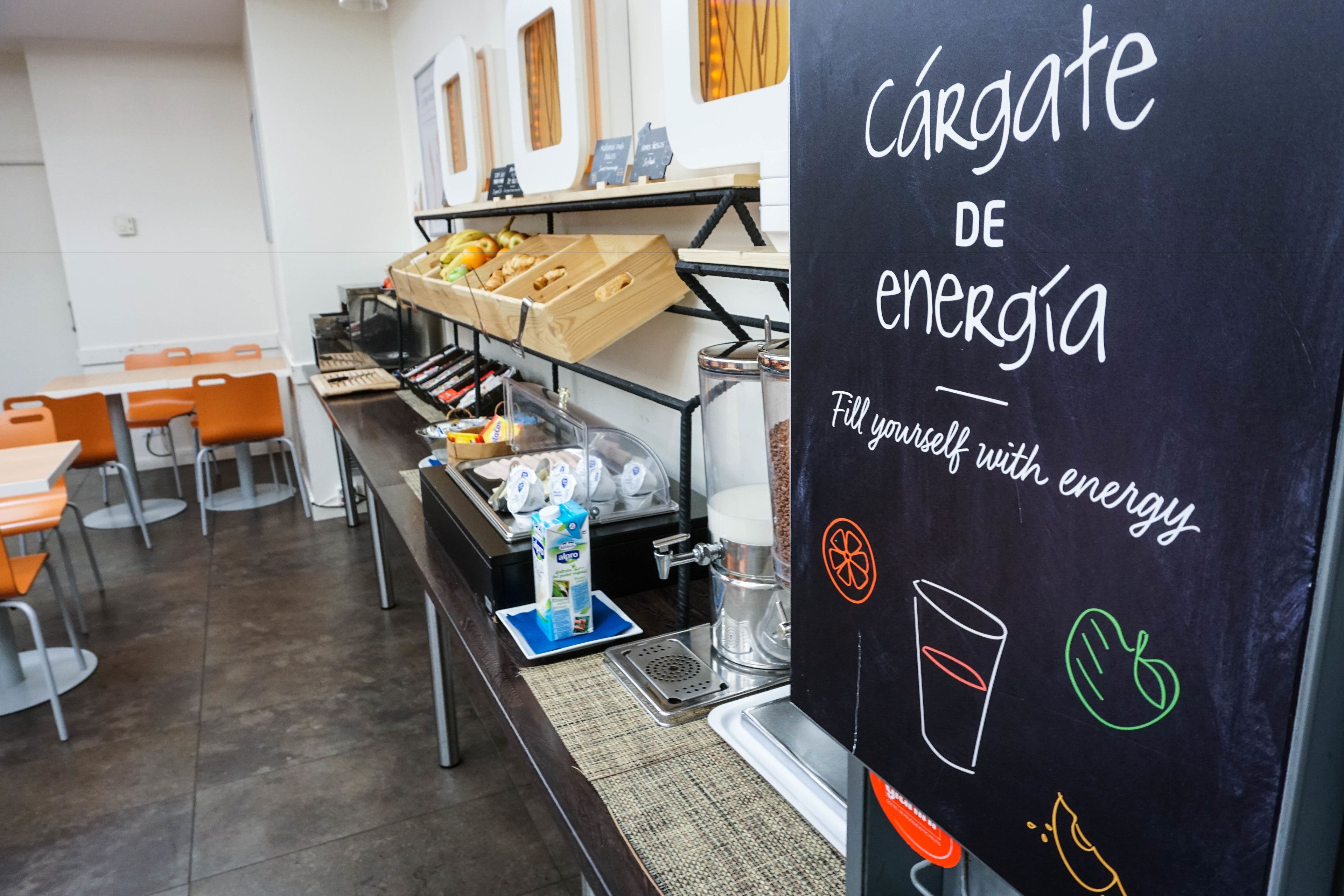 A breakfast area with a chalkboard sign reading "cárgate de energía" and a coffee machine.