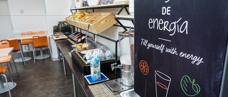 A breakfast area with a chalkboard sign reading "cárgate de energía" and a coffee machine.