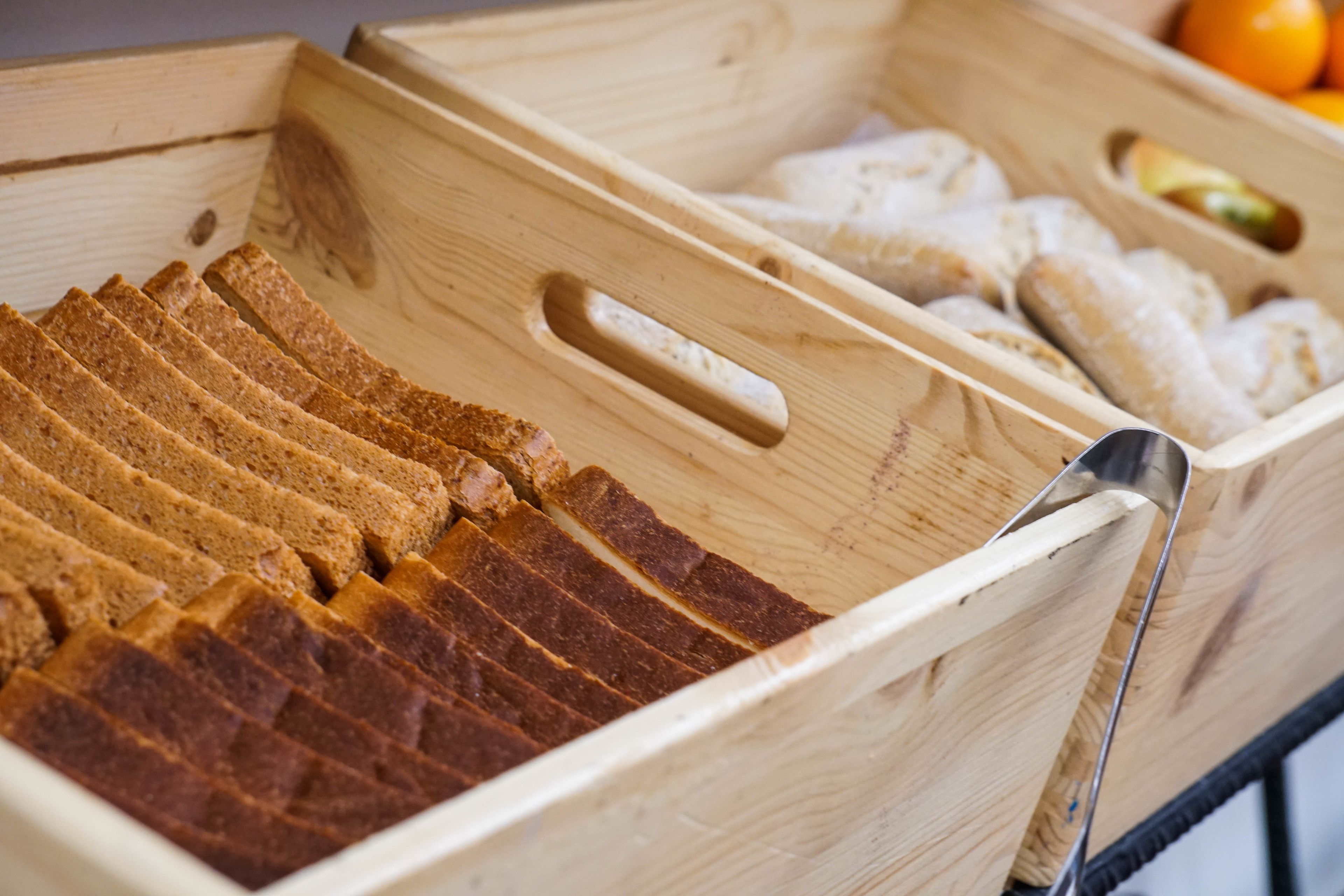 Una caja de madera con pan rebanado y una cuchara de metal.
