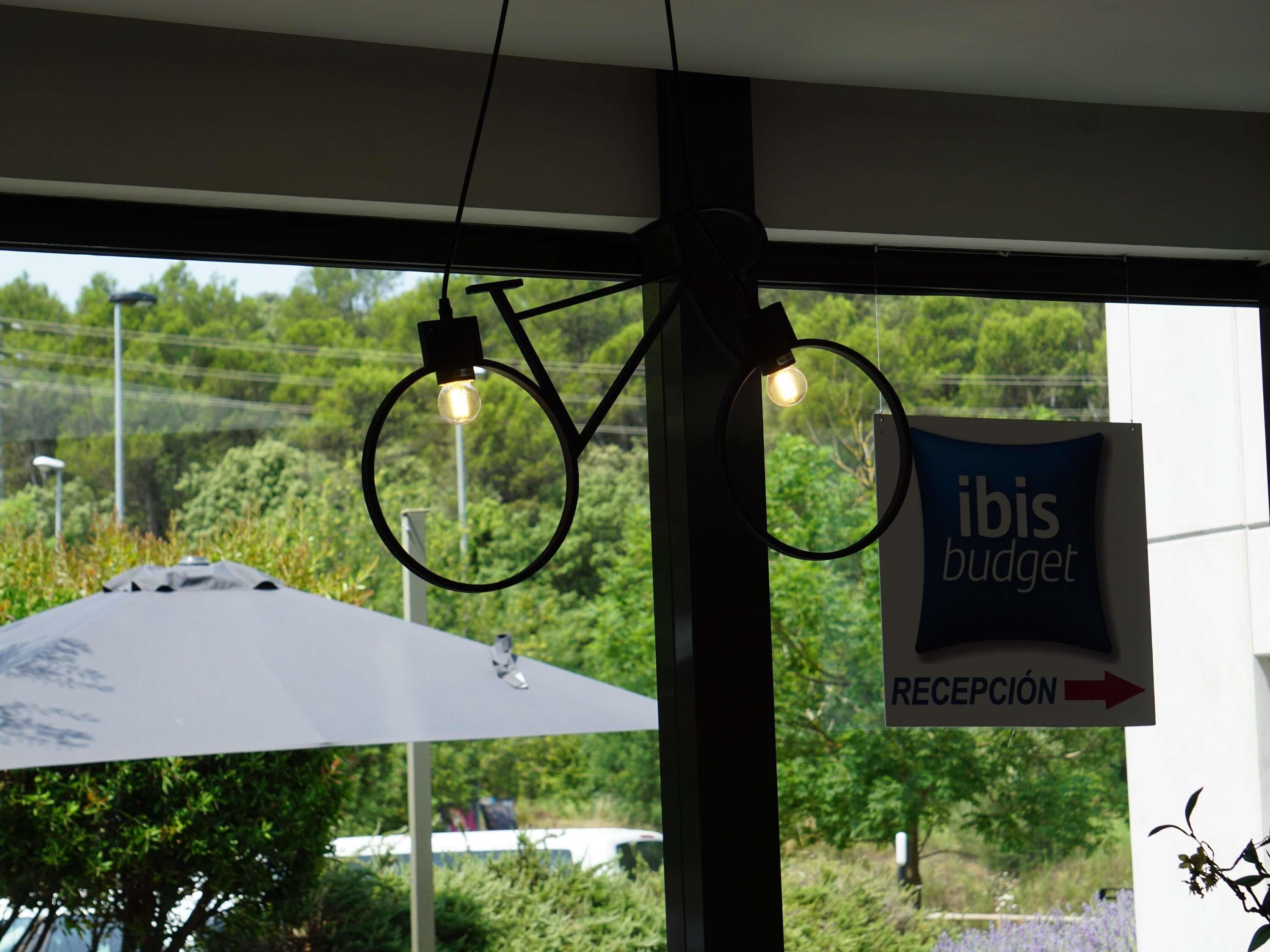Un área de recepción con un cartel que dice 'ibis budget' y una lámpara con forma de bicicleta.