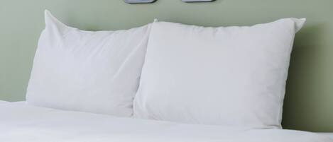A bed with white bedding and pillows, a green headboard, and two digital clocks above the headboard.