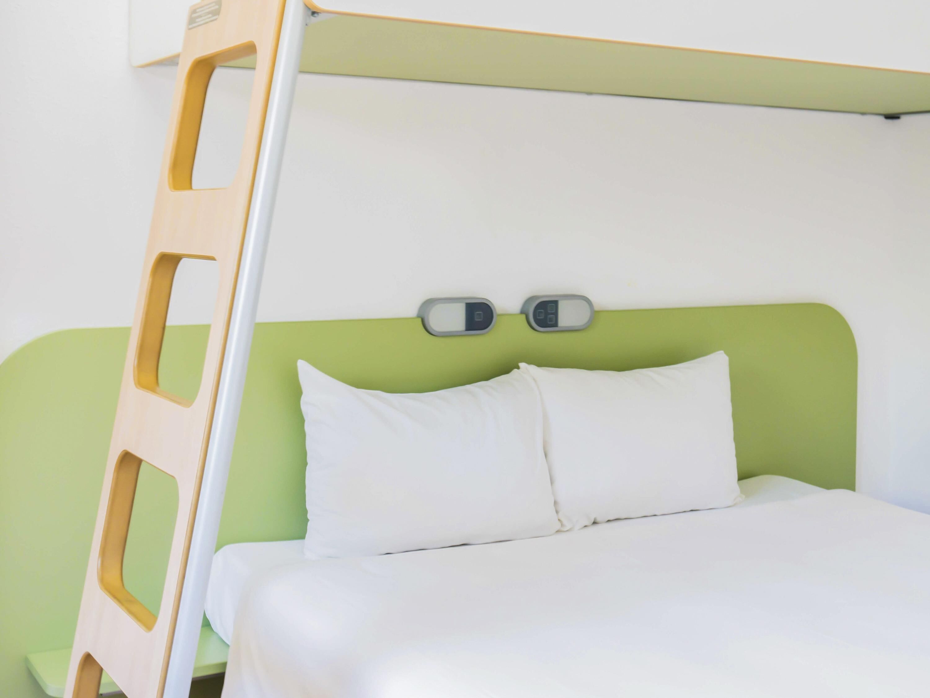 Una cama con ropa blanca, cabecera verde y dos controles junto a la cama.