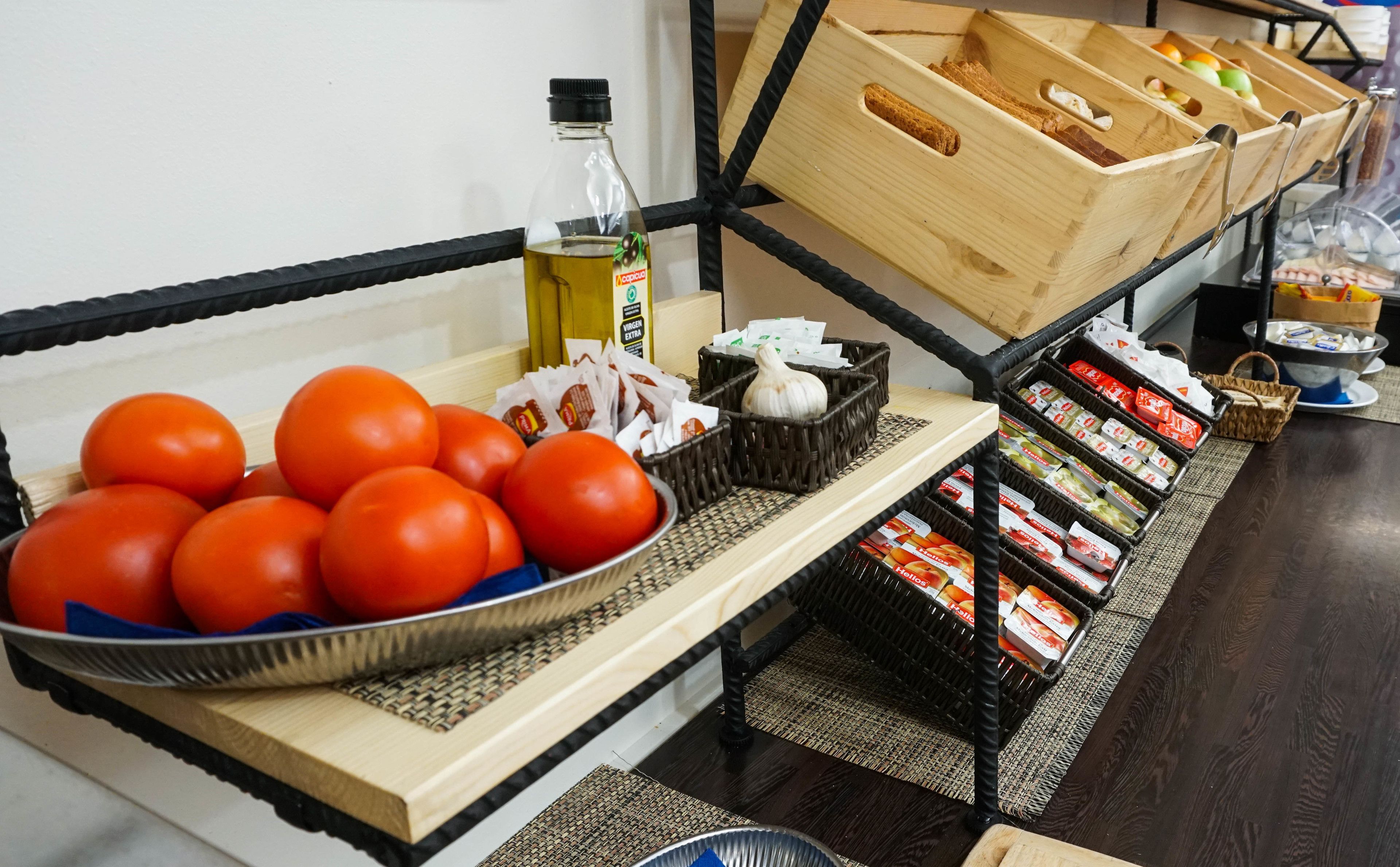 A kitchen counter with a bowl of tomatoes, a bottle of olive oil, and various packaged food items.