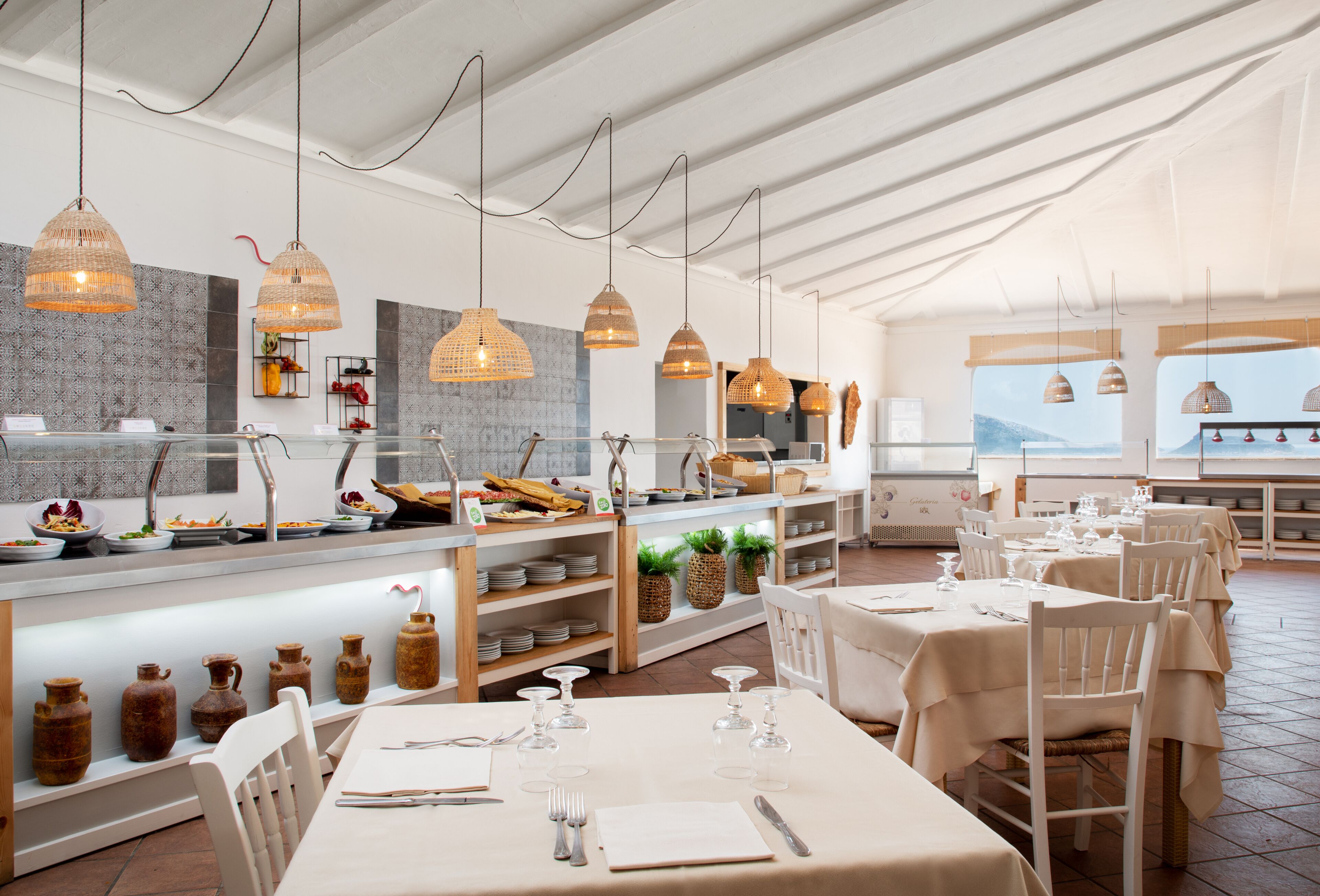 Een restaurant met een lange toonbank, hangende hanglampen en witte tafels.